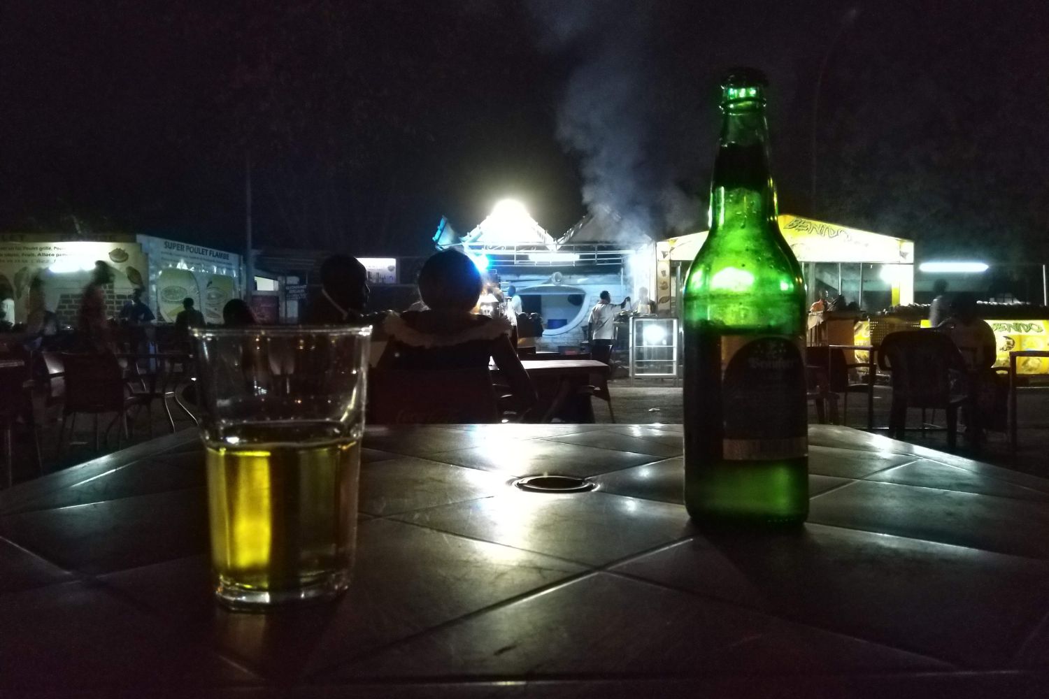 A table with a beer on it in an open-air buvette in West Africa